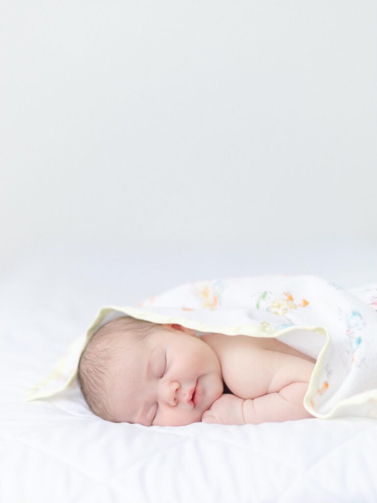 Cubby newborn baby sleeps on their belly under a lightweight blanket.