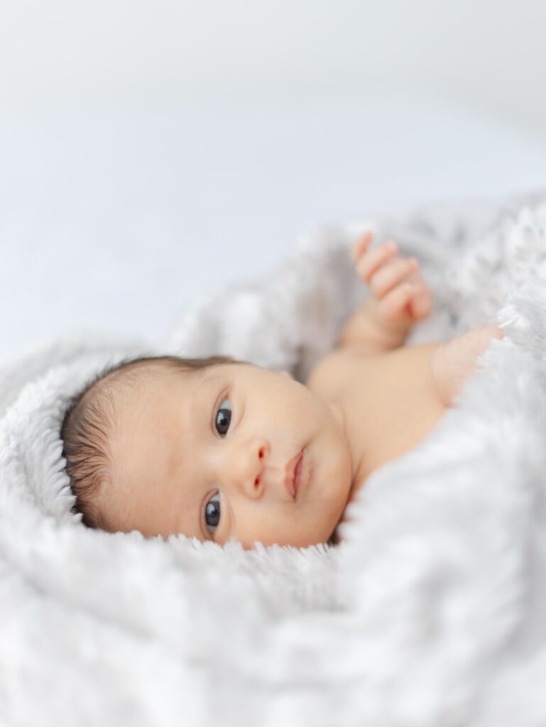 Newborn baby with dark hair and eyes is wrapped in a fuzzy soft white blanket.